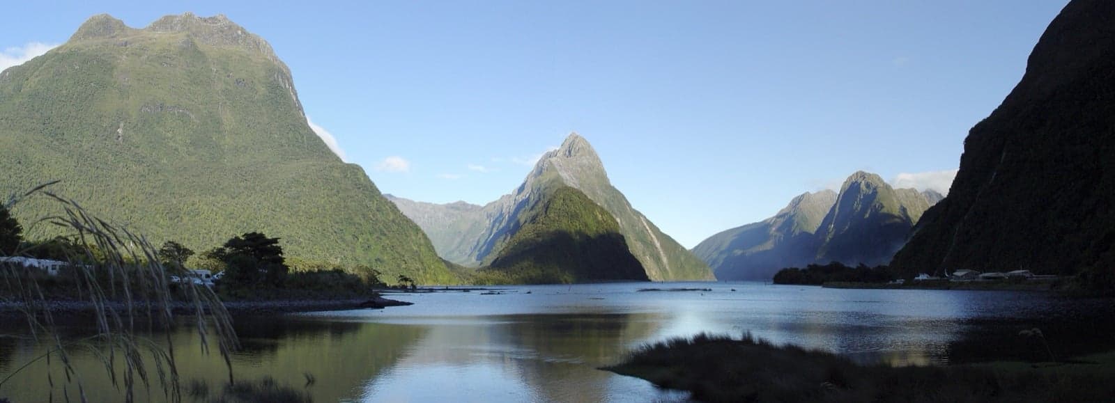 Steep green mountains rising out of the still water of Milford Sound, New Zealand