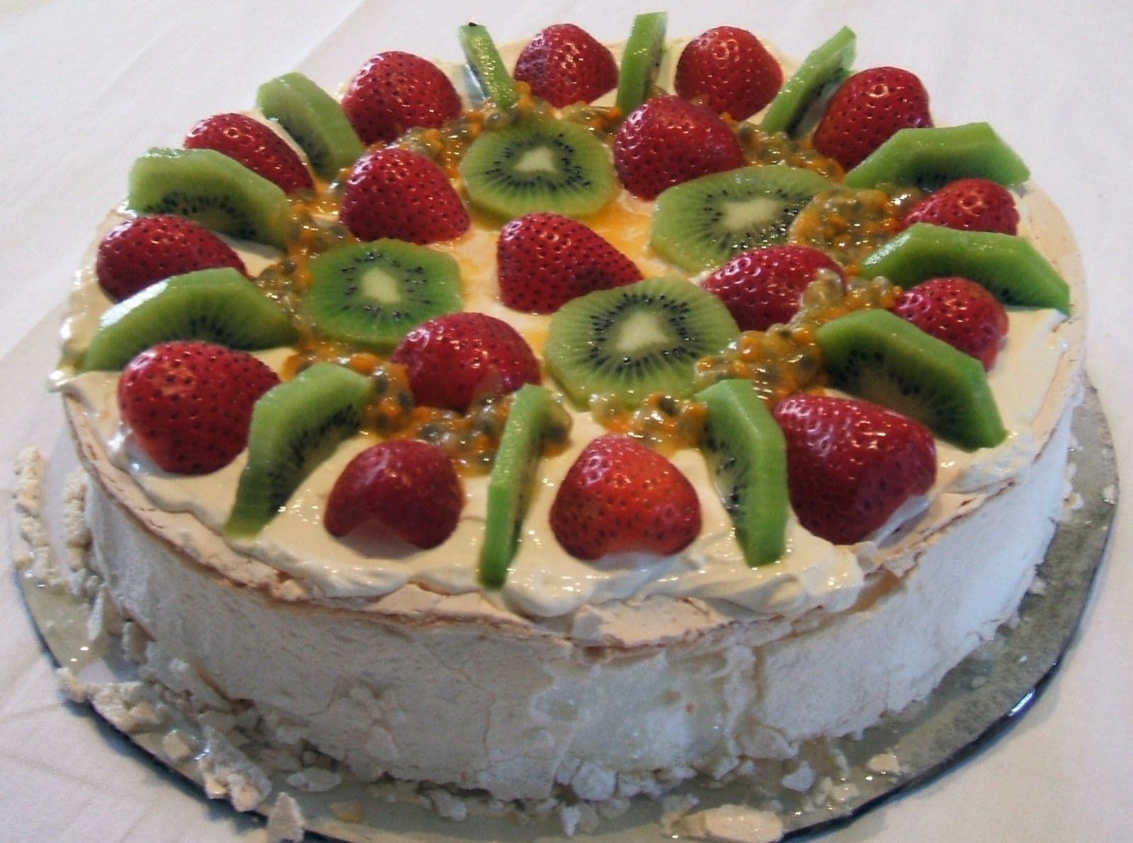 A round pavlova dessert topped with whipped cream, strawberries, kiwifruit and passionfruit