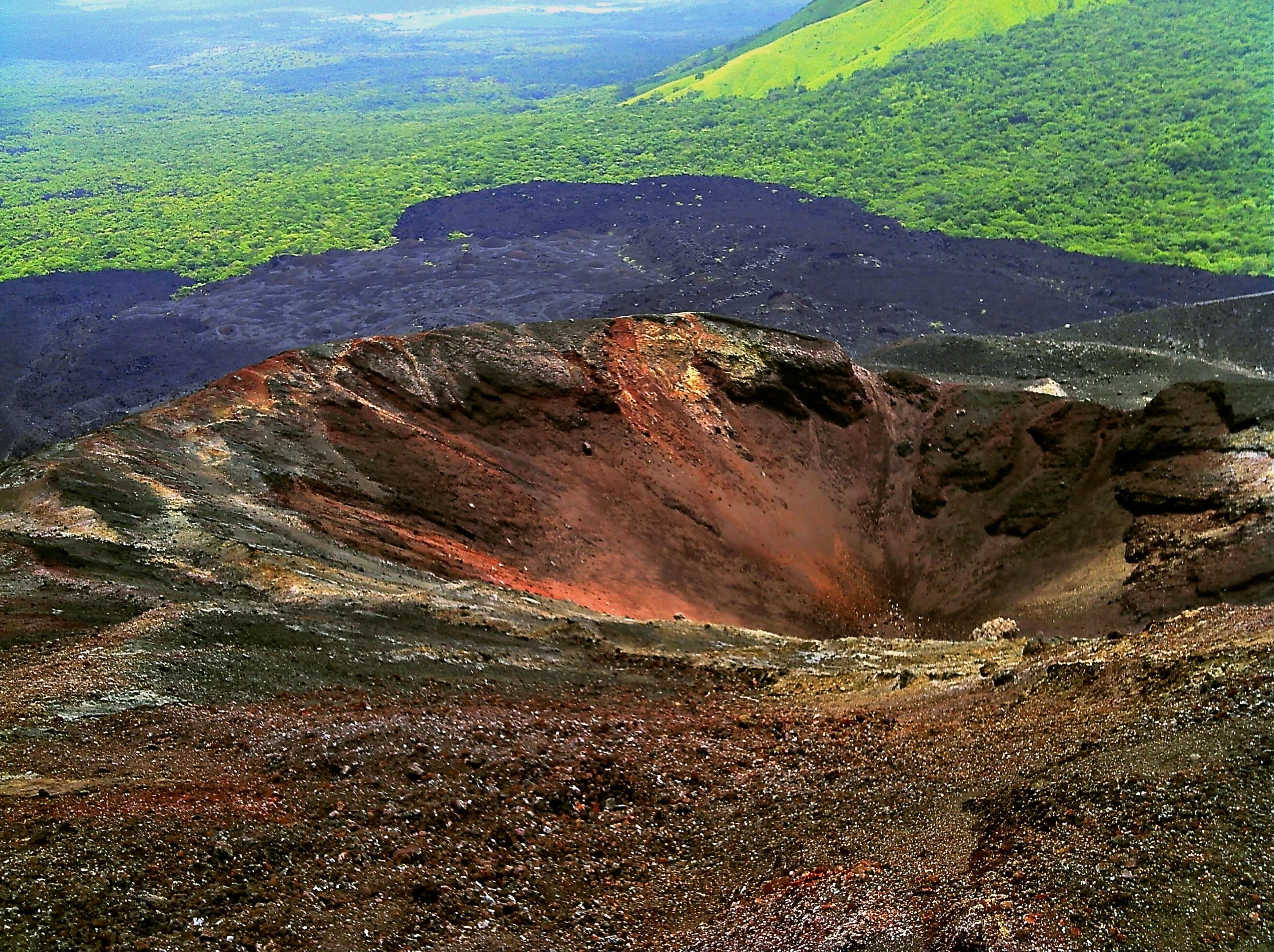 A person on a wooden board racing down the black ash slope of Cerro Negro volcano