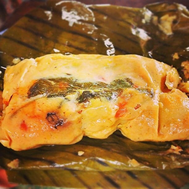 A nacatamal unwrapped from its banana leaf, showing the corn dough filling with pork and rice