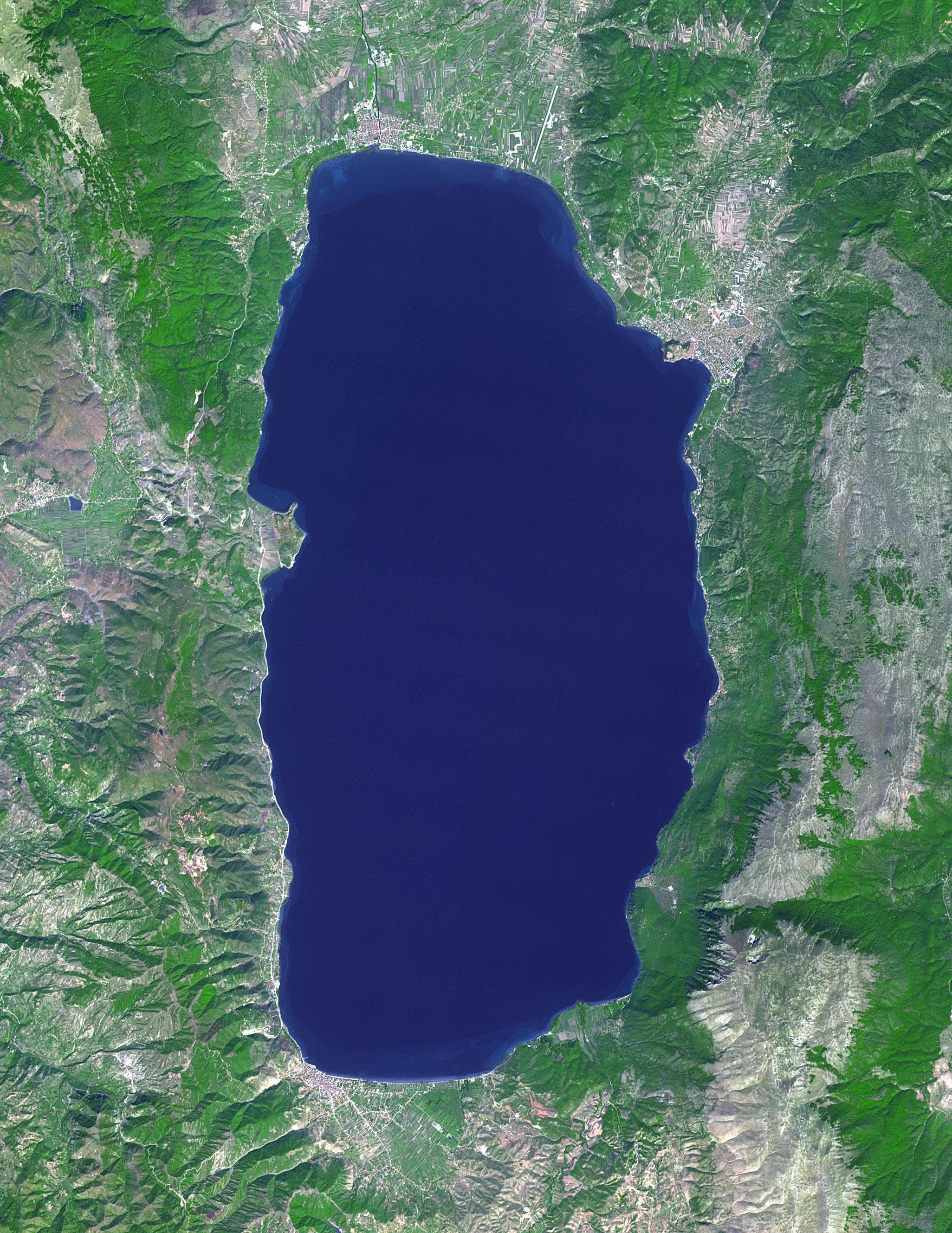 Calm blue waters of Lake Ohrid with mountains in the background and a small church on the shore