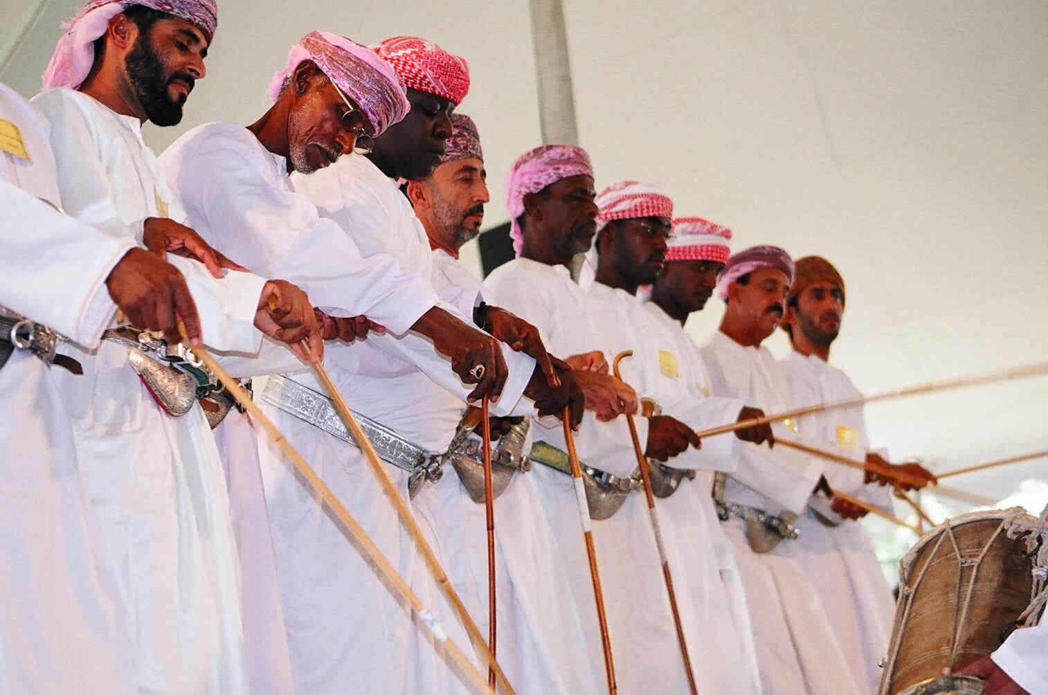 Omani men in traditional white robes performing the Razha sword dance with decorated swords