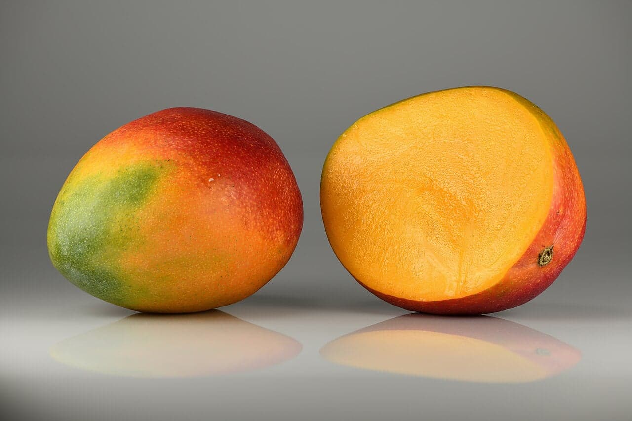 Two mangoes - one whole and one cut in half showing the bright orange flesh