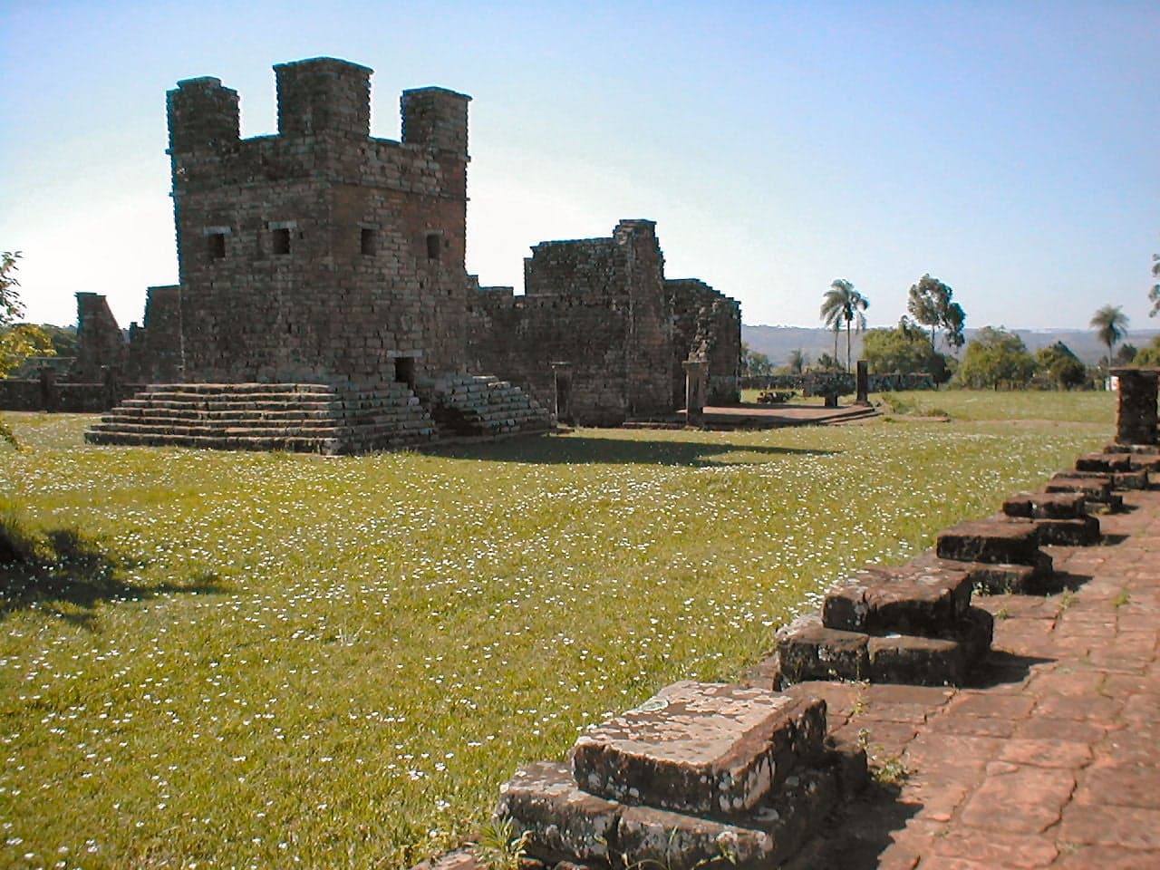 Carved stone archways and columns of a Jesuit mission ruin surrounded by green jungle