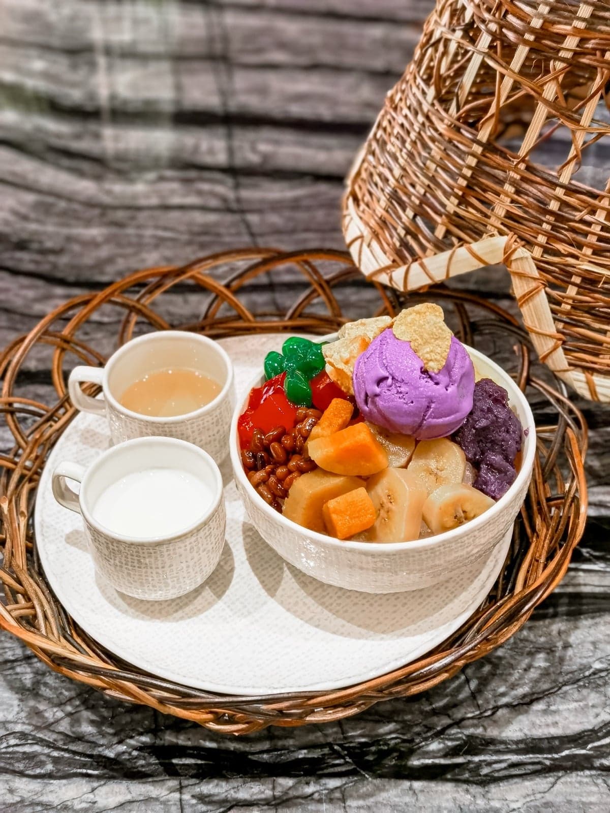 A bowl of halo-halo with purple ube ice cream, bananas, sweet beans, jelly and red cherries