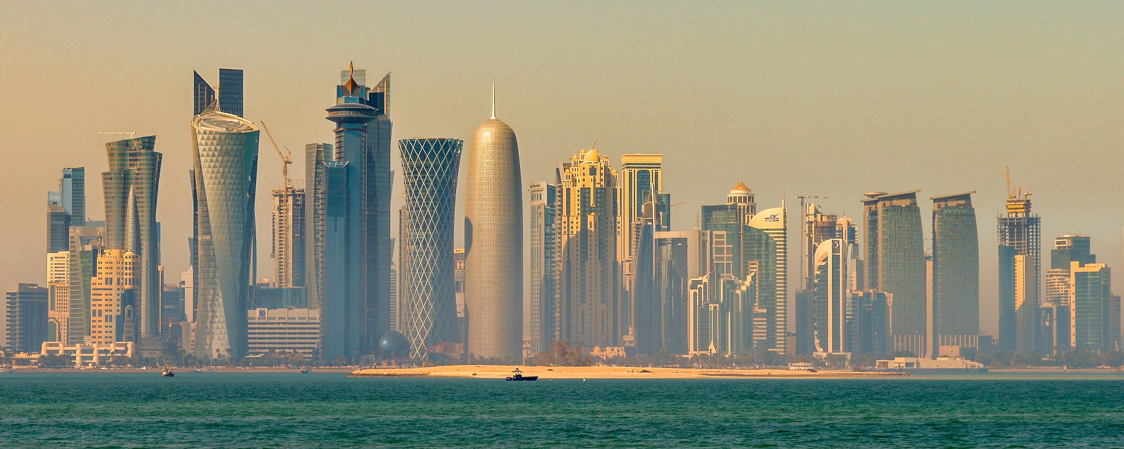 The glittering towers of Doha reflected in the calm waters of the Corniche at dusk