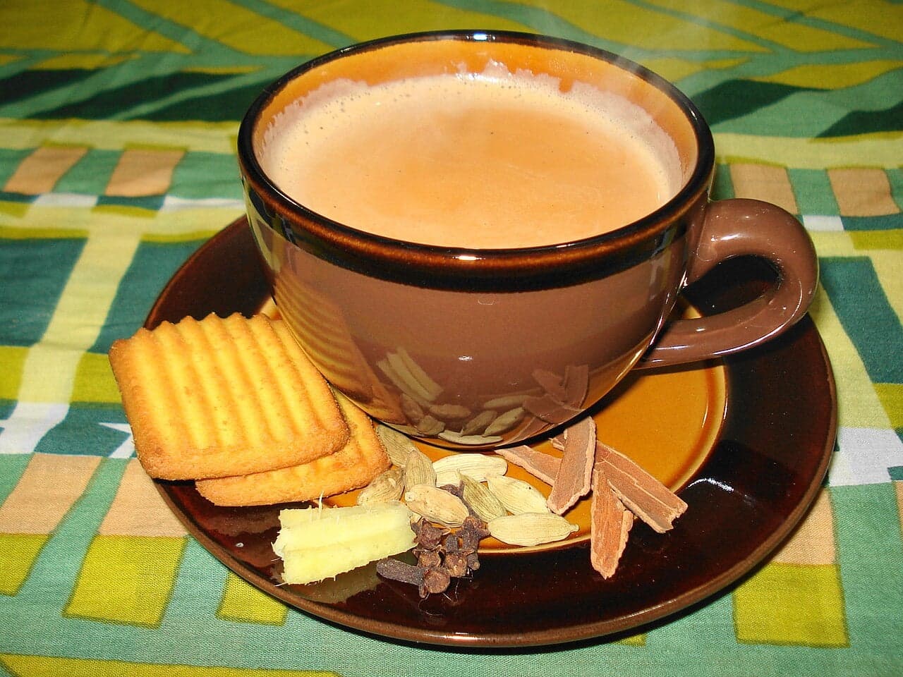 Two small glass cups of rich golden karak chai on a wooden tray with cardamom pods