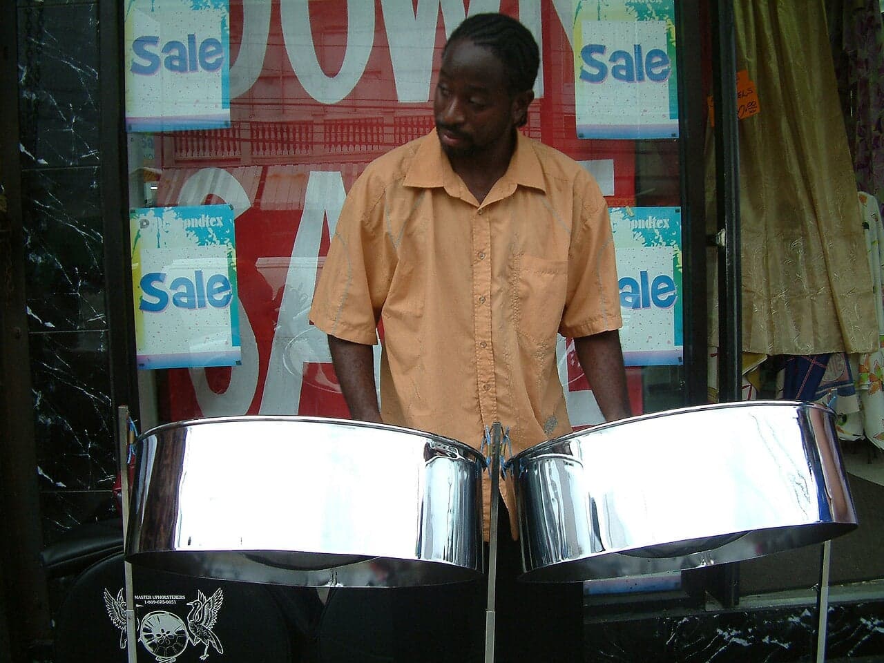 A musician playing a shiny silver steelpan drum outdoors in the Caribbean
