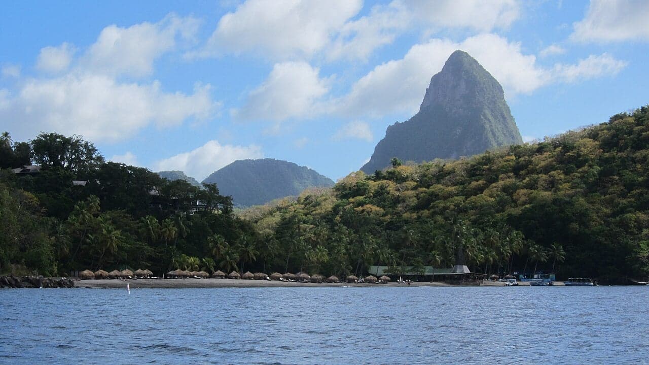 A crescent of dark volcanic sand beach backed by dense green rainforest and blue Caribbean water