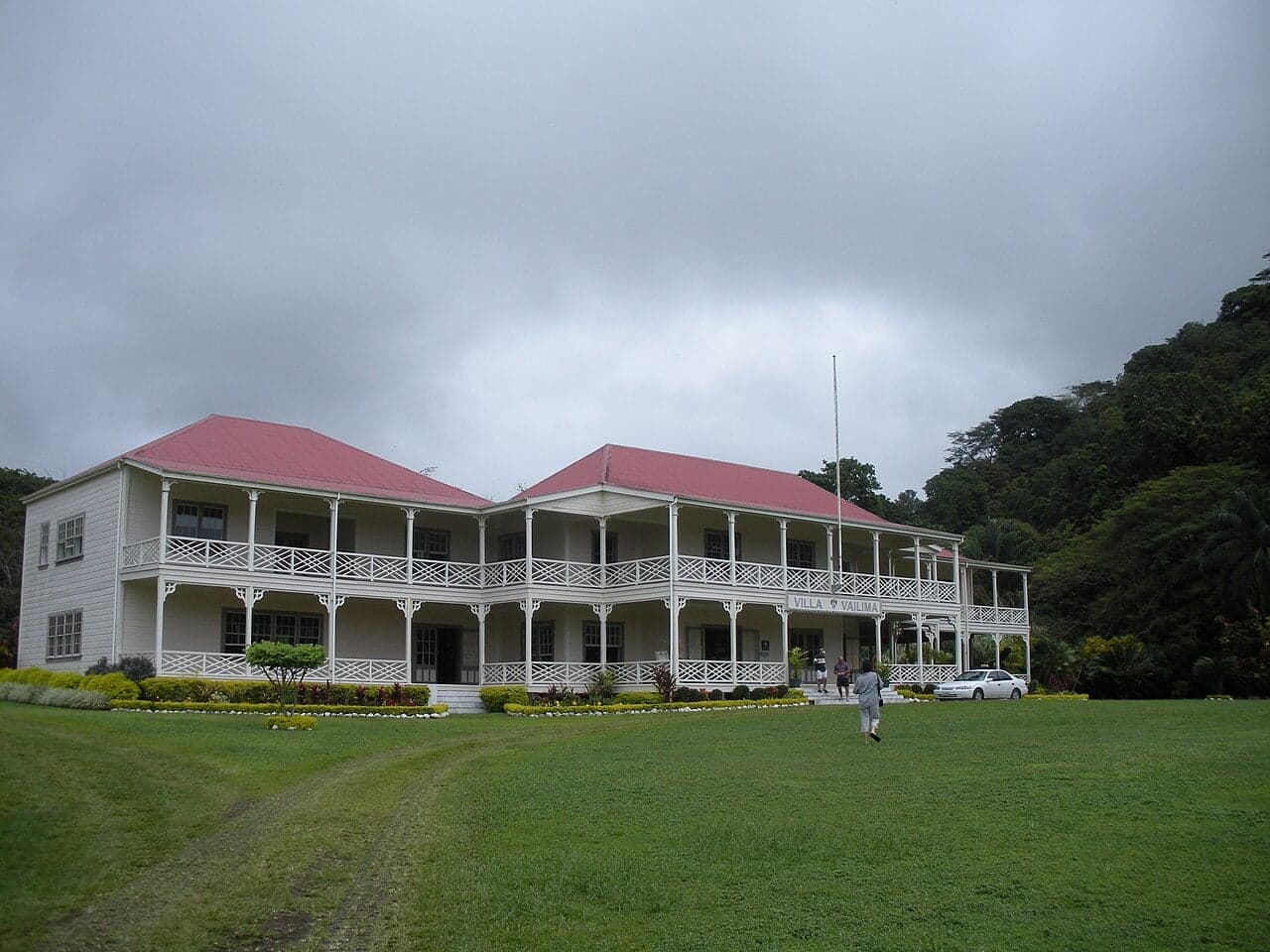 A large white colonial house surrounded by tropical trees and gardens