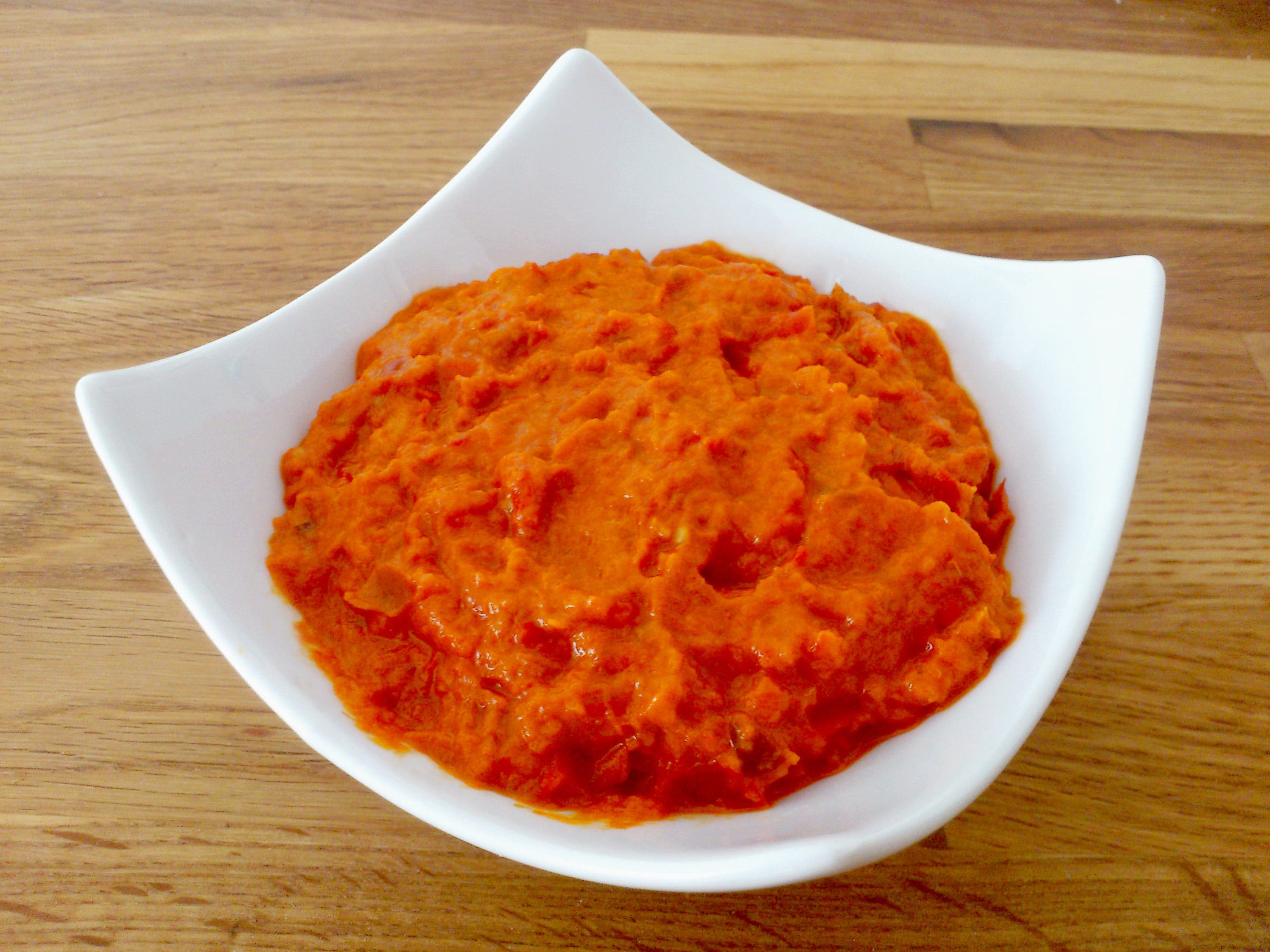 A glass jar of bright red ajvar pepper spread with bread on the side