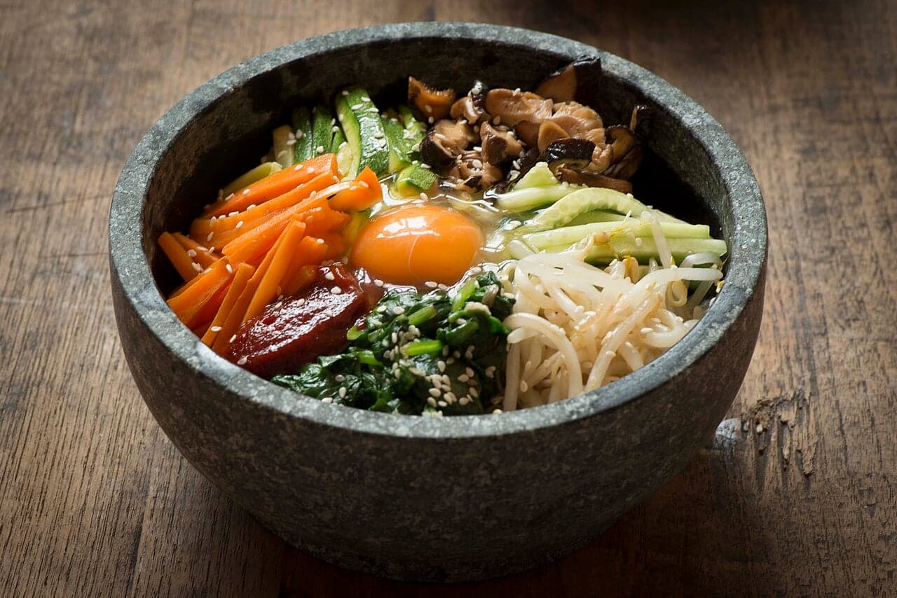 A bowl of bibimbap with rice, carrots, mushrooms, spinach, bean sprouts and an egg yolk