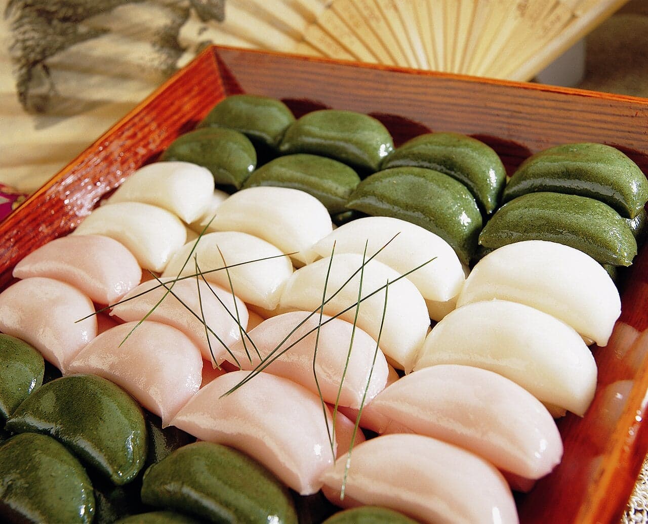 A box of brightly coloured pink, white and green half-moon rice cakes called songpyeon