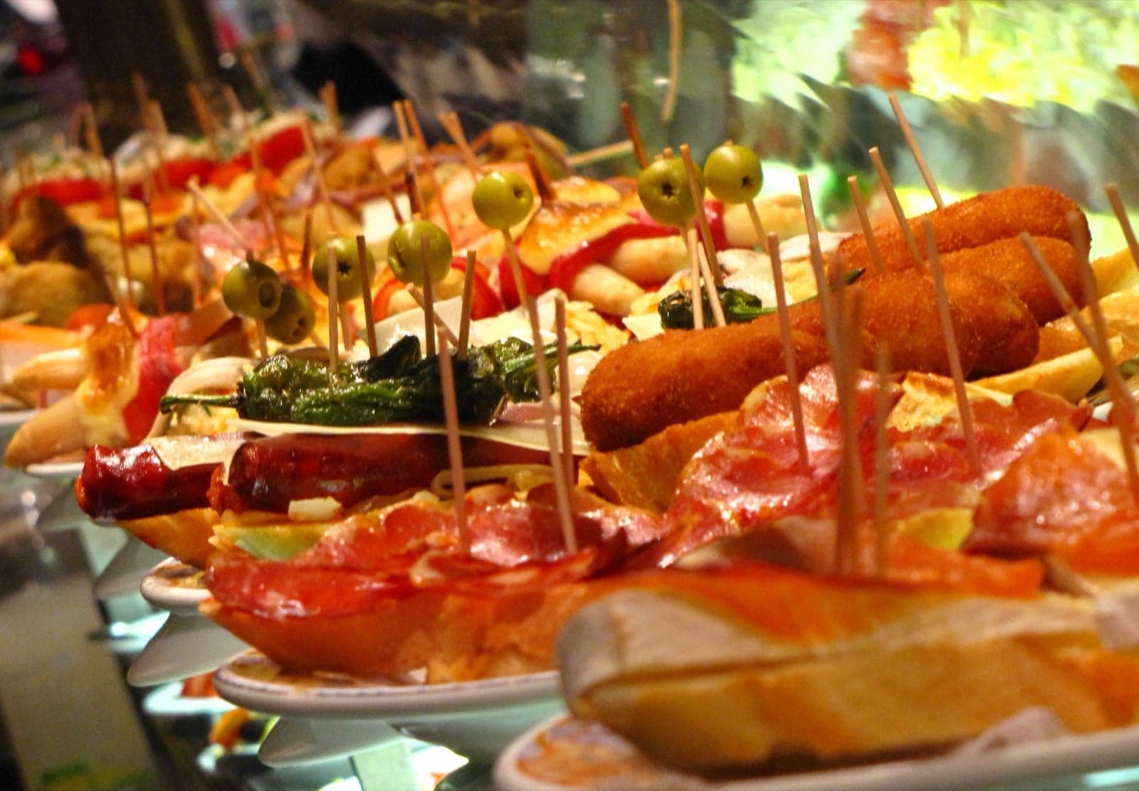 A bar counter covered in colourful Spanish tapas, including tomato bread, jamón and croquetas