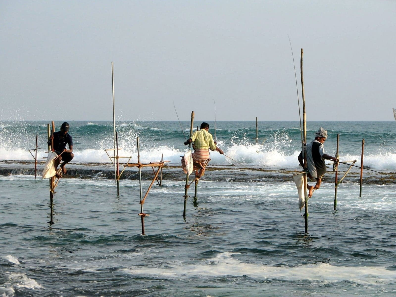 Three stilt fishermen perched on poles in the surf near Unawatuna, Sri Lanka