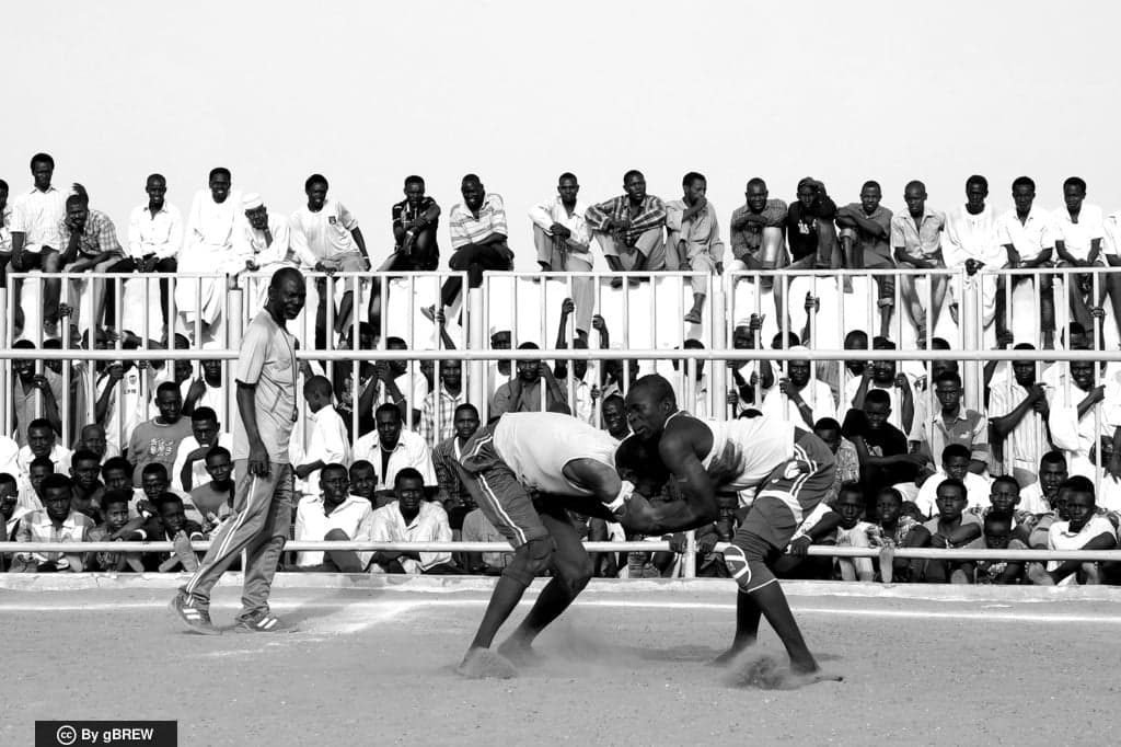 Two Nuba wrestlers competing in a sandy arena surrounded by celebrating spectators