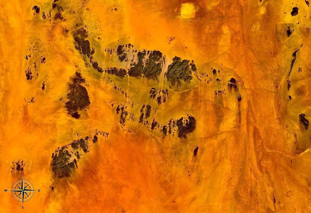 Golden sand dunes and bare rock ridges of the Nubian Desert under a bright blue sky