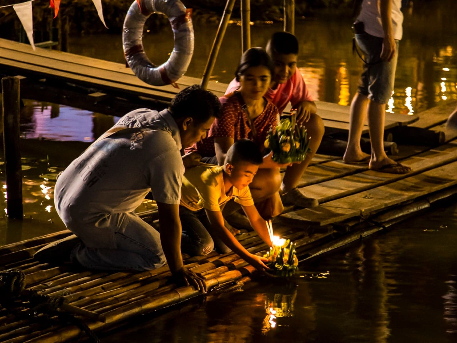 A family setting a candlelit krathong on the water at Loi Krathong