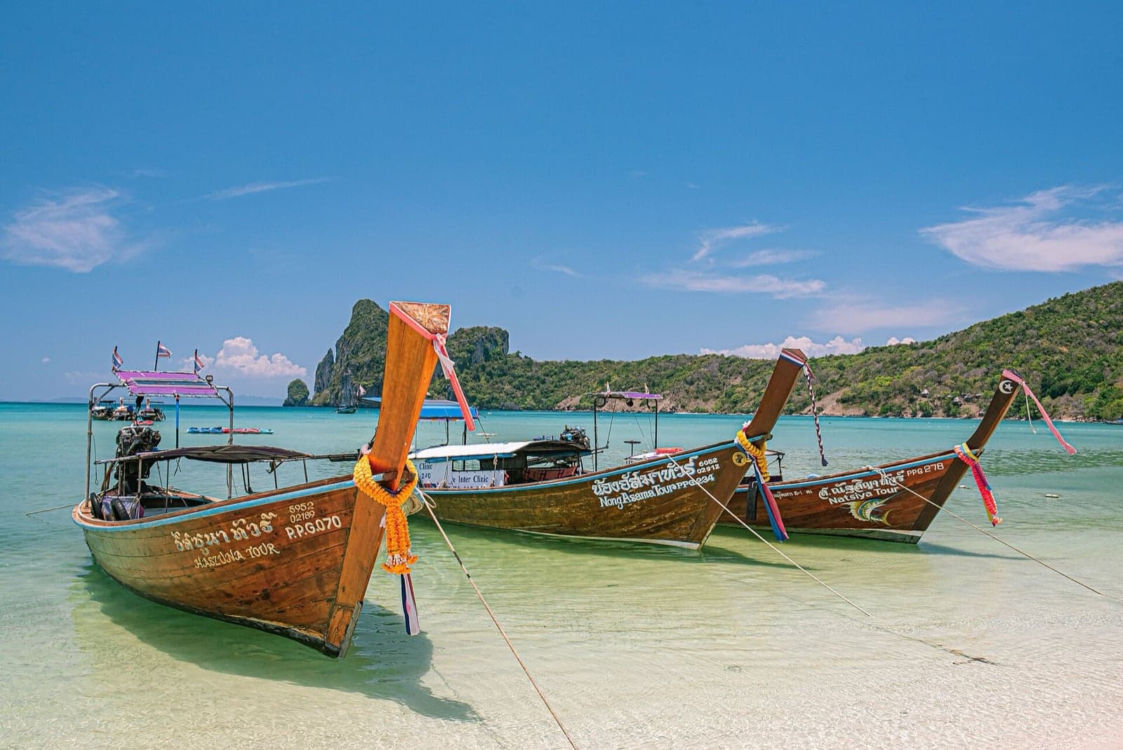 Wooden longtail boats with colourful garlands moored on a clear-water beach in Krabi