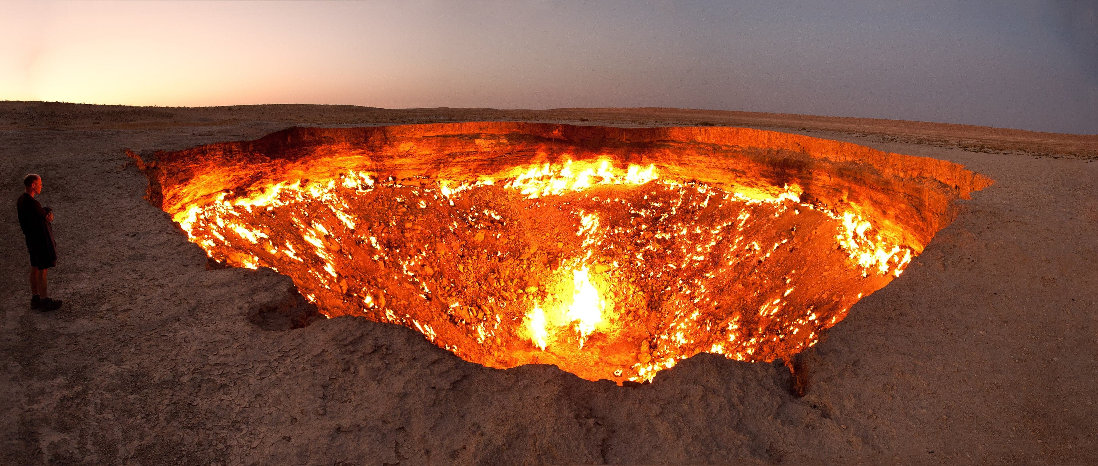 The Darvaza crater glowing bright orange with flames at night in the Karakum Desert