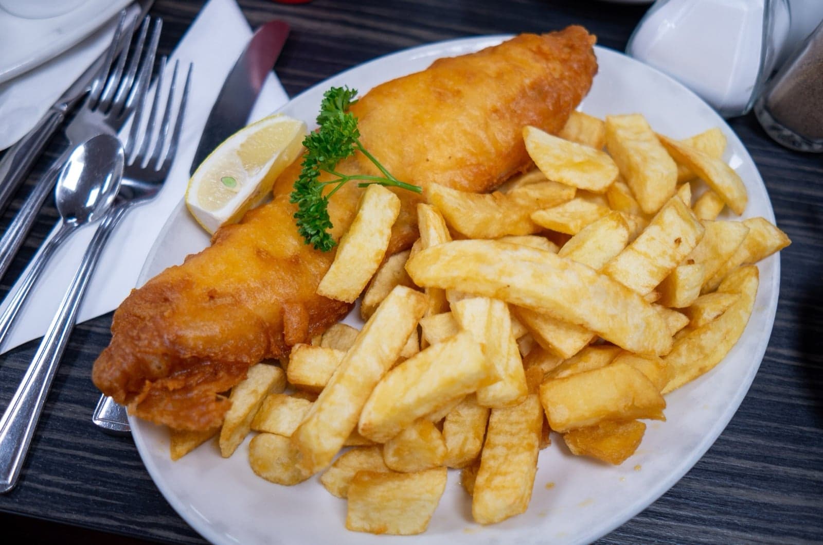 A plate of golden battered fish and thick-cut chips with a wedge of lemon