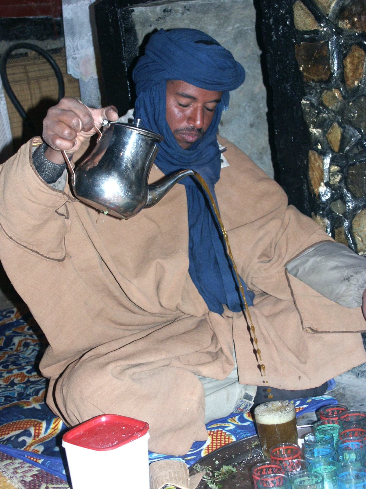 Small decorative glasses of bright green tea being poured with a frothy stream