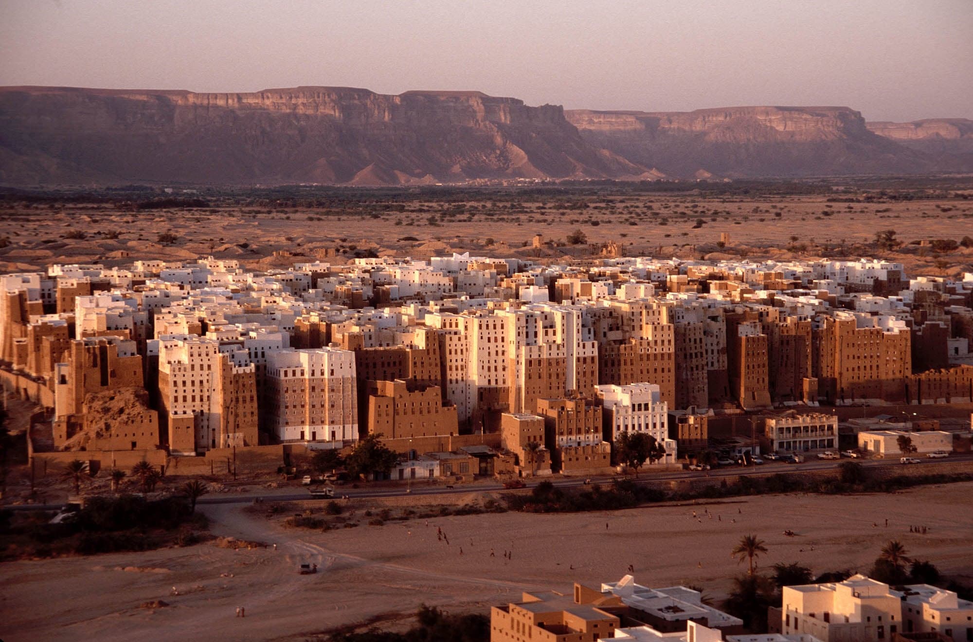 A wadi village of mud-brick houses nestled at the base of towering sandstone cliffs in Hadhramaut