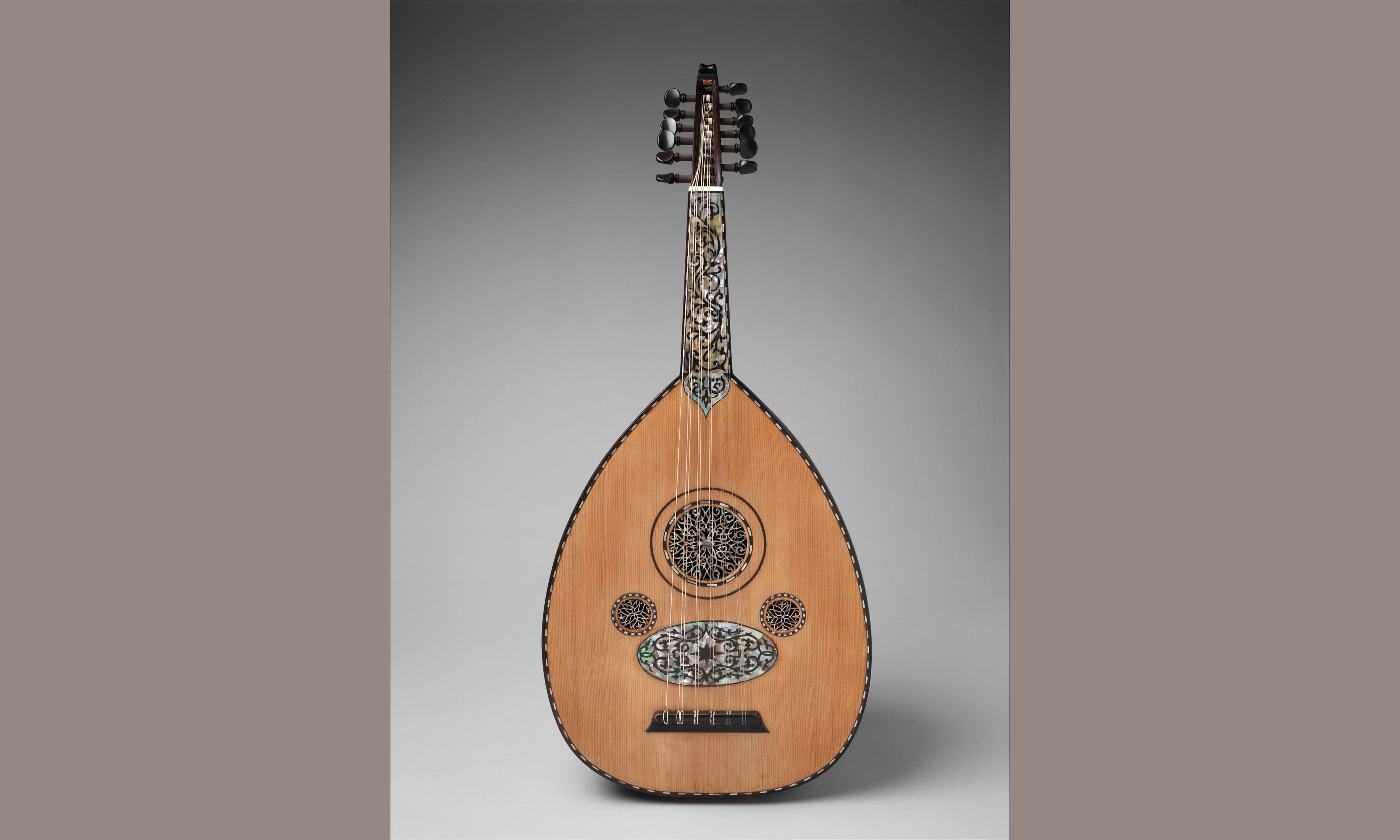 A craftsman holding a beautifully finished oud with its distinctive round wooden body and short neck