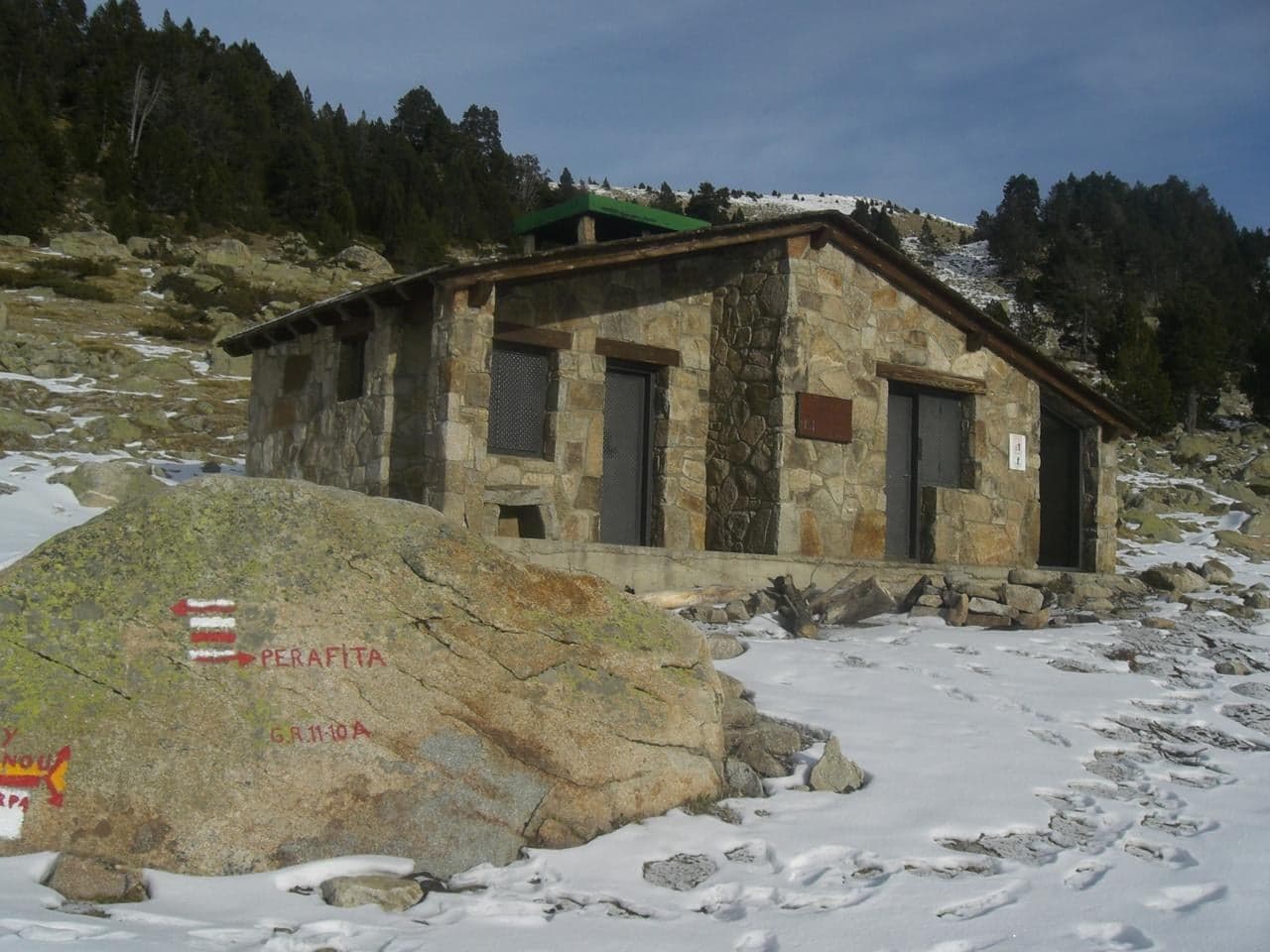 A wide mountain valley with a clear blue lake and rocky peaks above it in Andorra