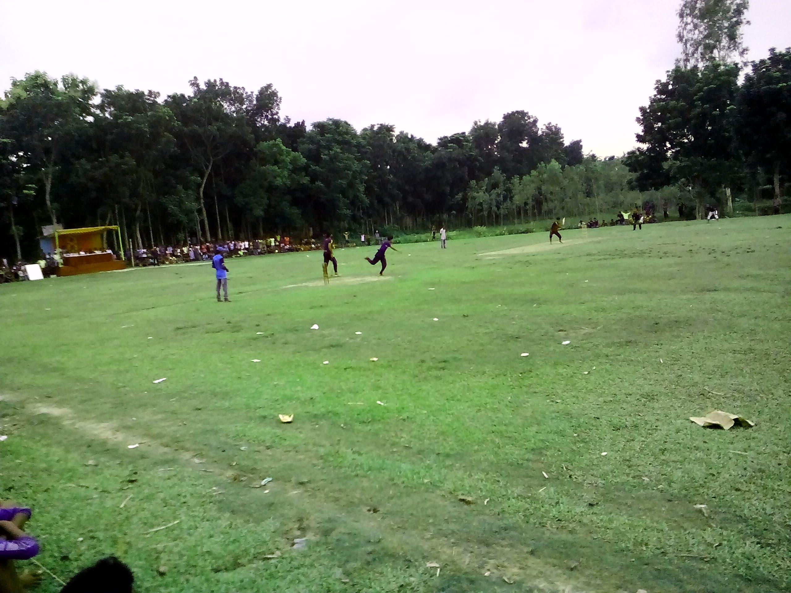 Children playing a cricket match on a grassy field in Bangladesh
