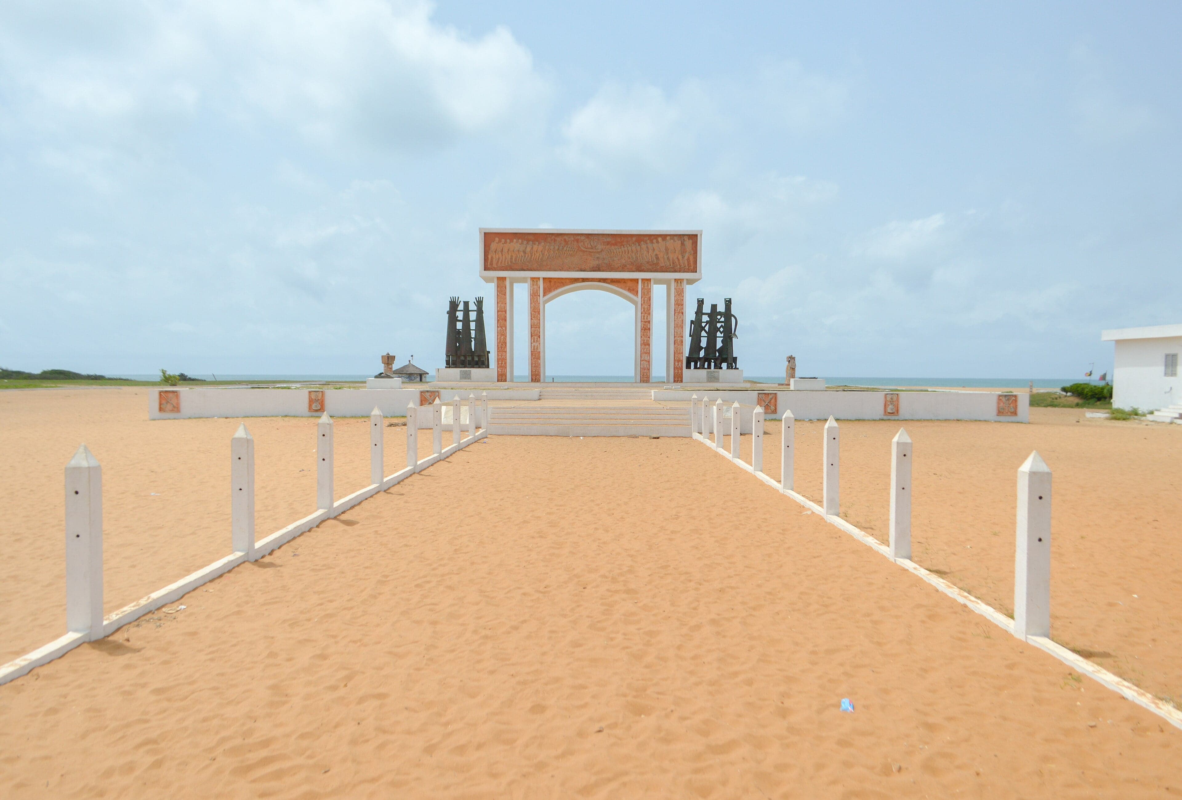 The colourful arch of the Door of No Return monument standing on the beach at Ouidah with the Atlantic Ocean behind it