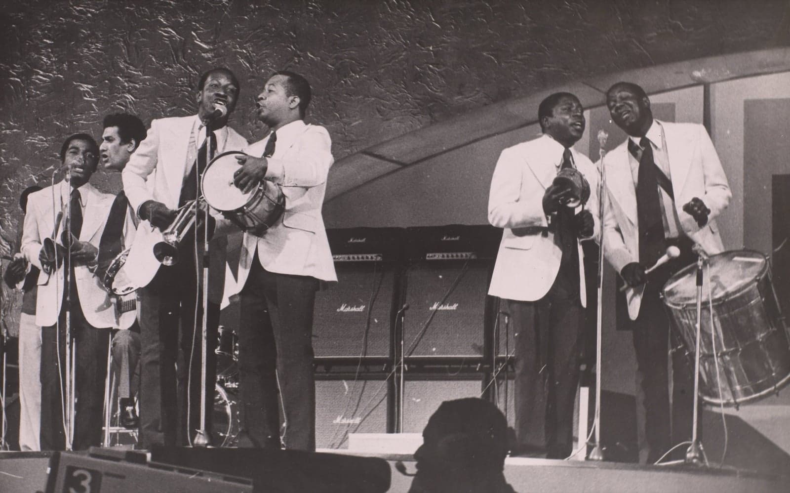 A samba group performing on stage with drums and microphones