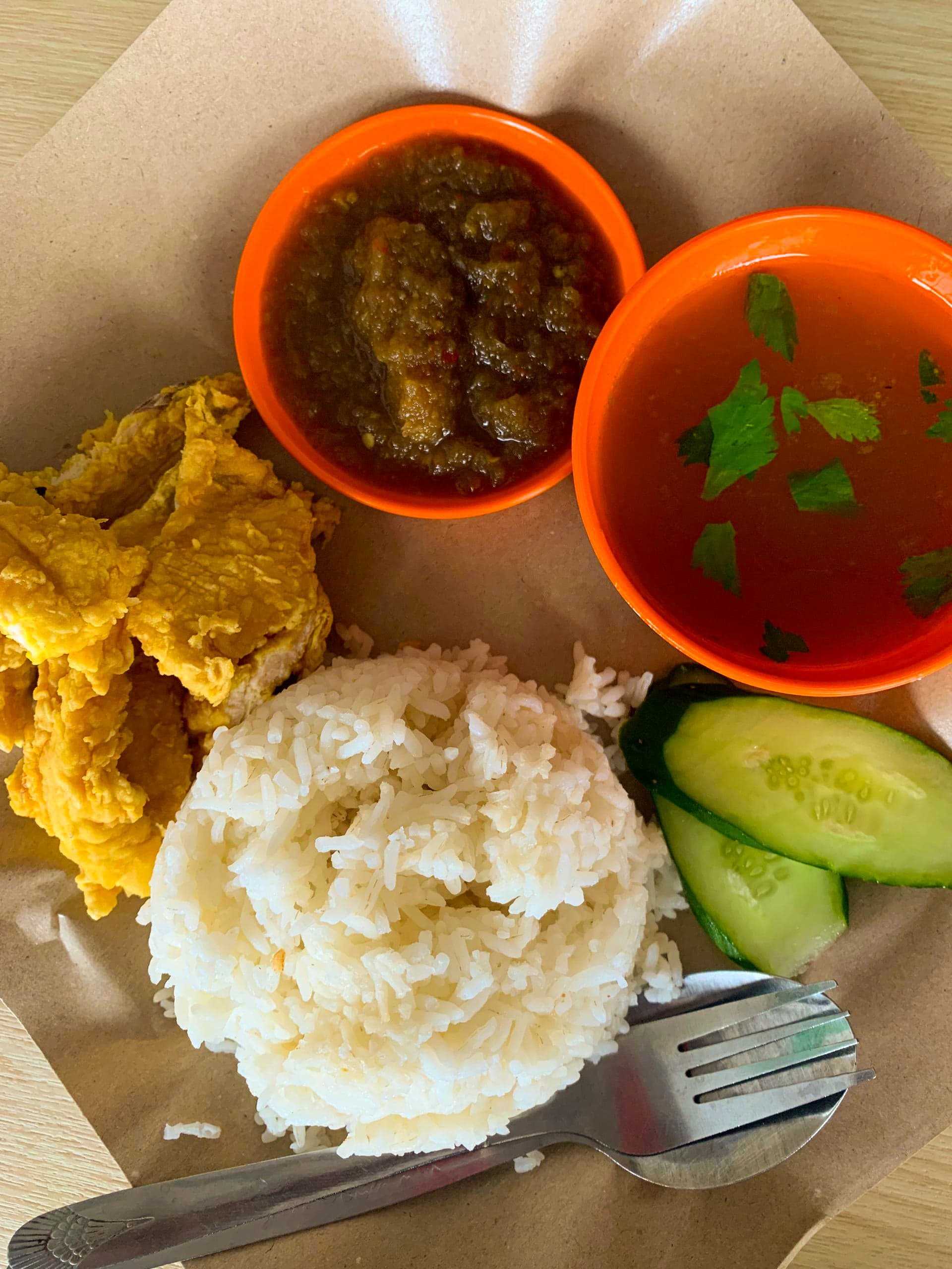 A portion of nasi katok - rice with fried chicken and red sambal wrapped in brown paper