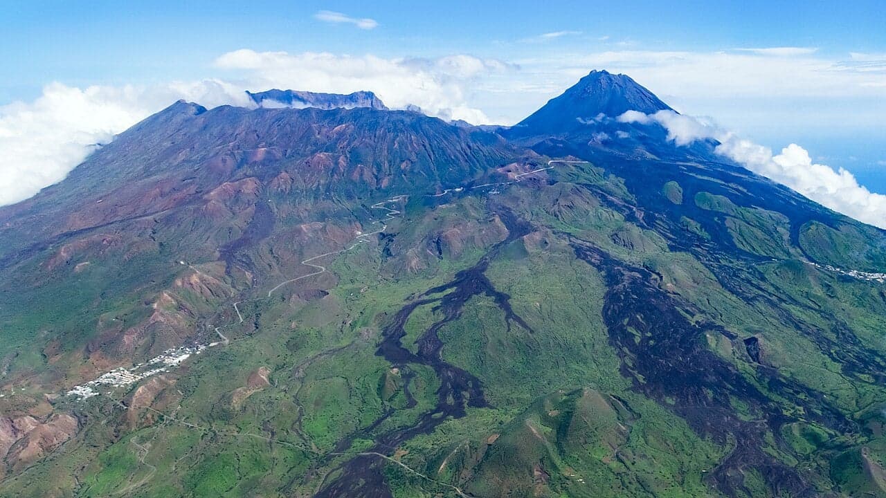 A bird's-eye view of a rocky green volcanic island rising out of bright blue Atlantic water