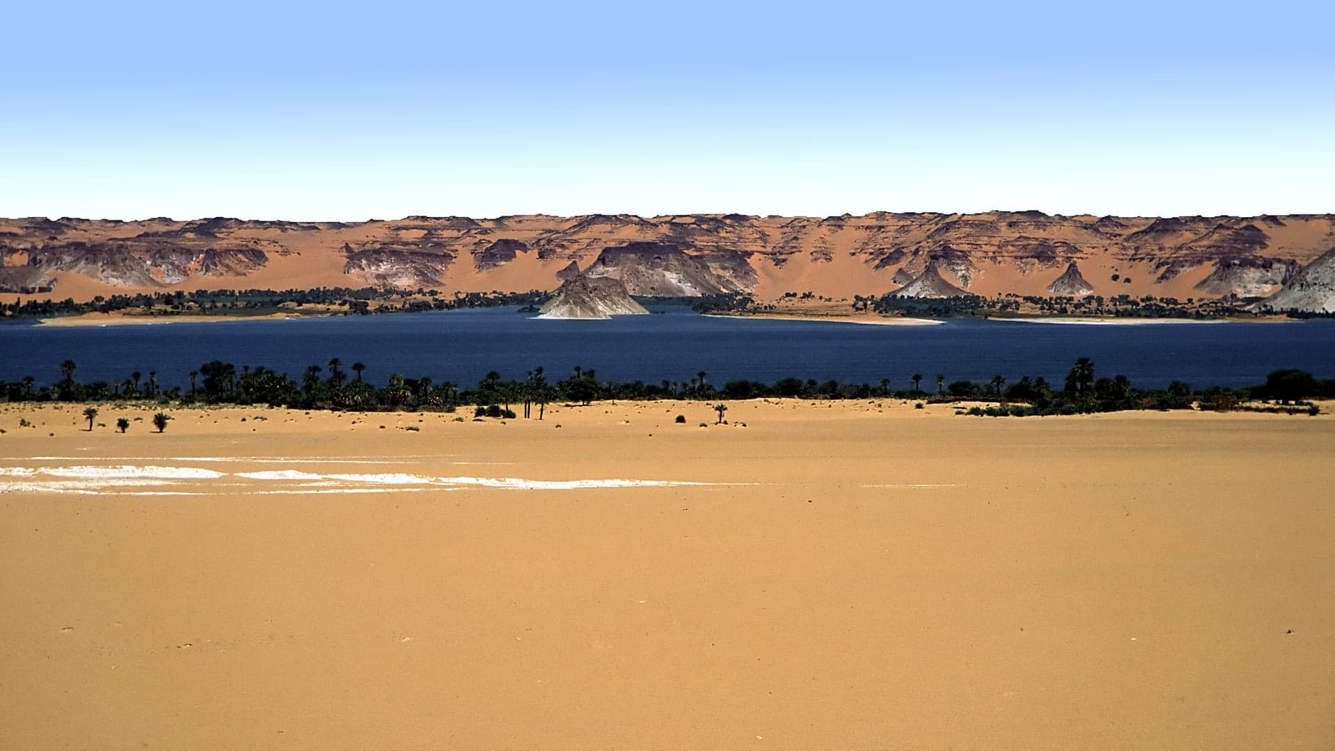 Vivid turquoise and green lakes surrounded by golden sand dunes and date palms at Ounianga