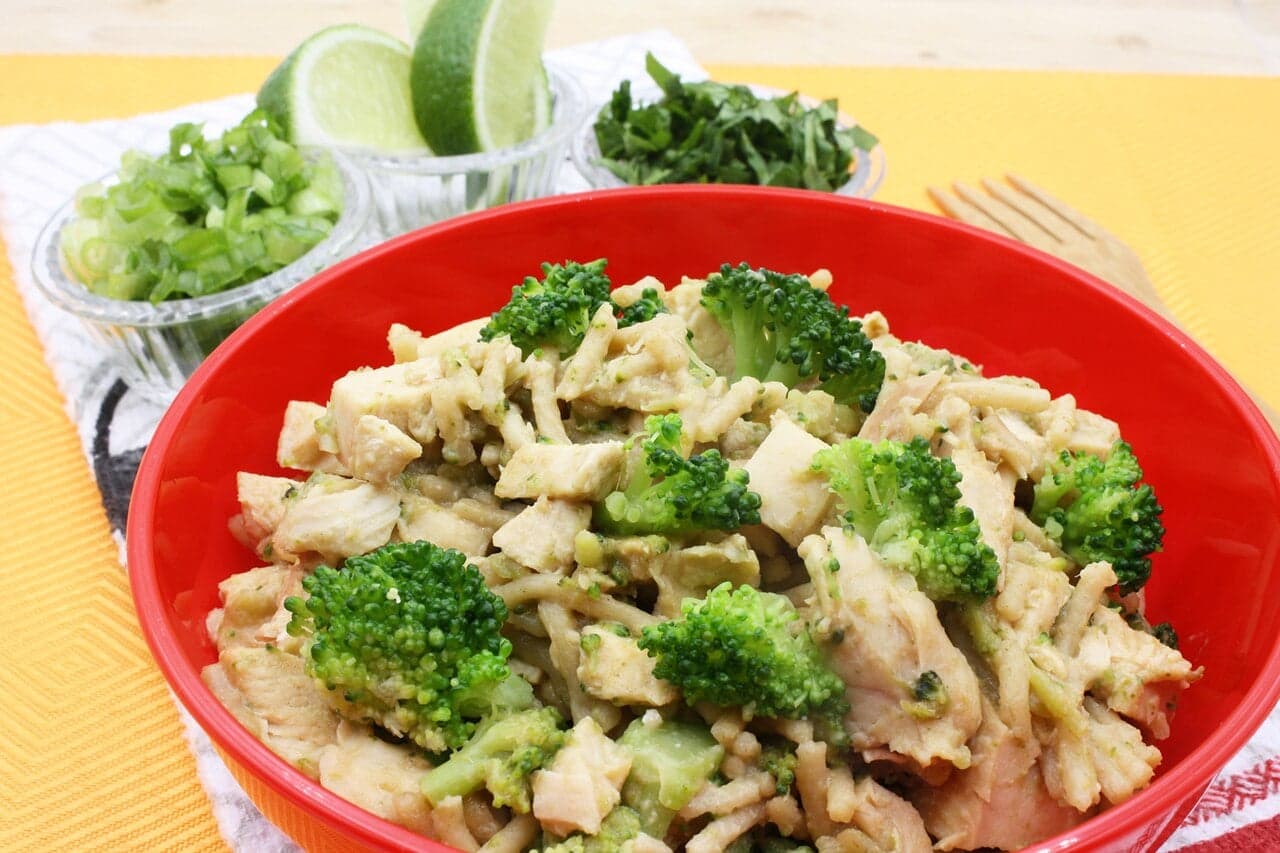 A bowl of golden peanut sauce with herbs, served alongside rice and vegetables