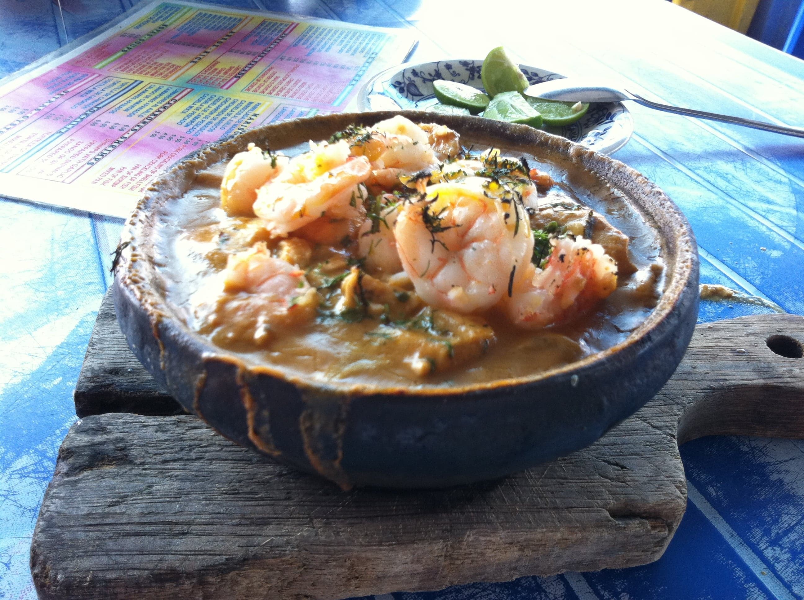 A clay bowl of Chilean cazuela filled with a golden broth, chicken, pumpkin, potato and corn on the cob