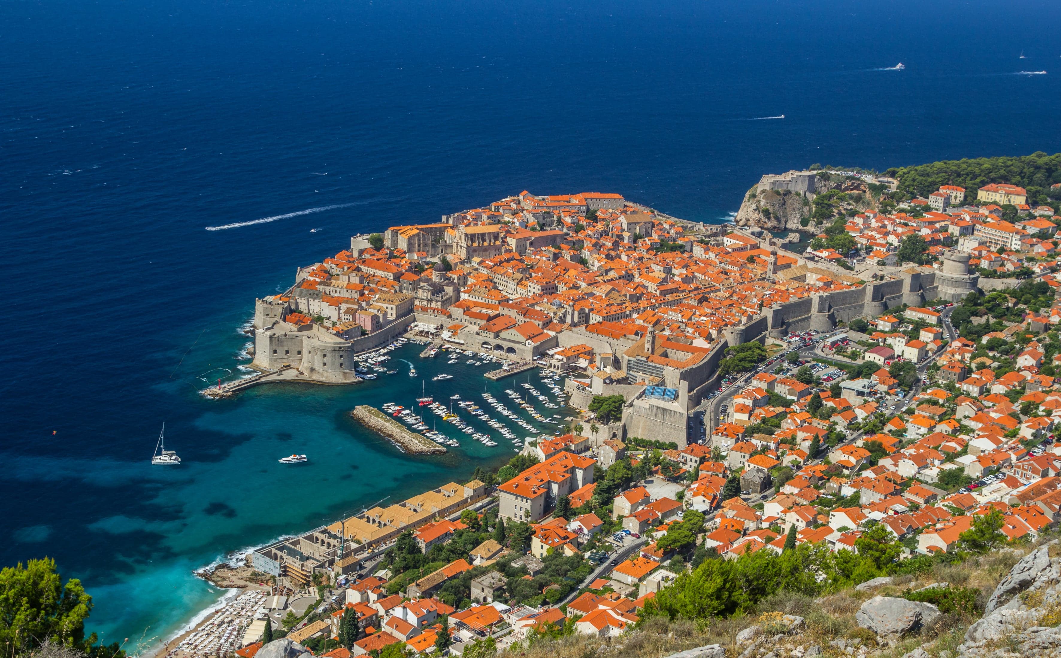 The orange-roofed old town of Dubrovnik surrounded by stone walls with the sea beyond