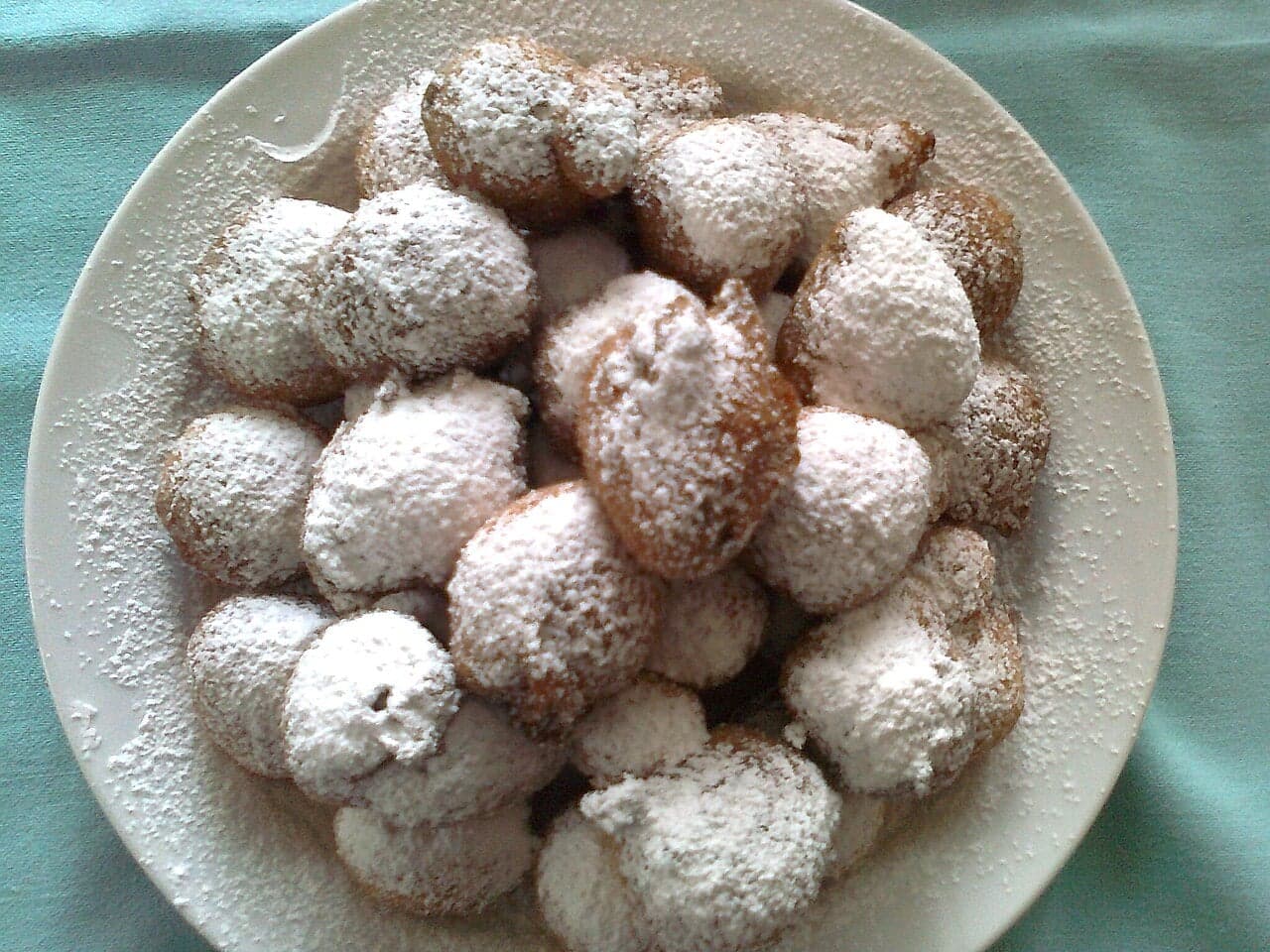 A pile of golden fritule dusted with icing sugar on a plate