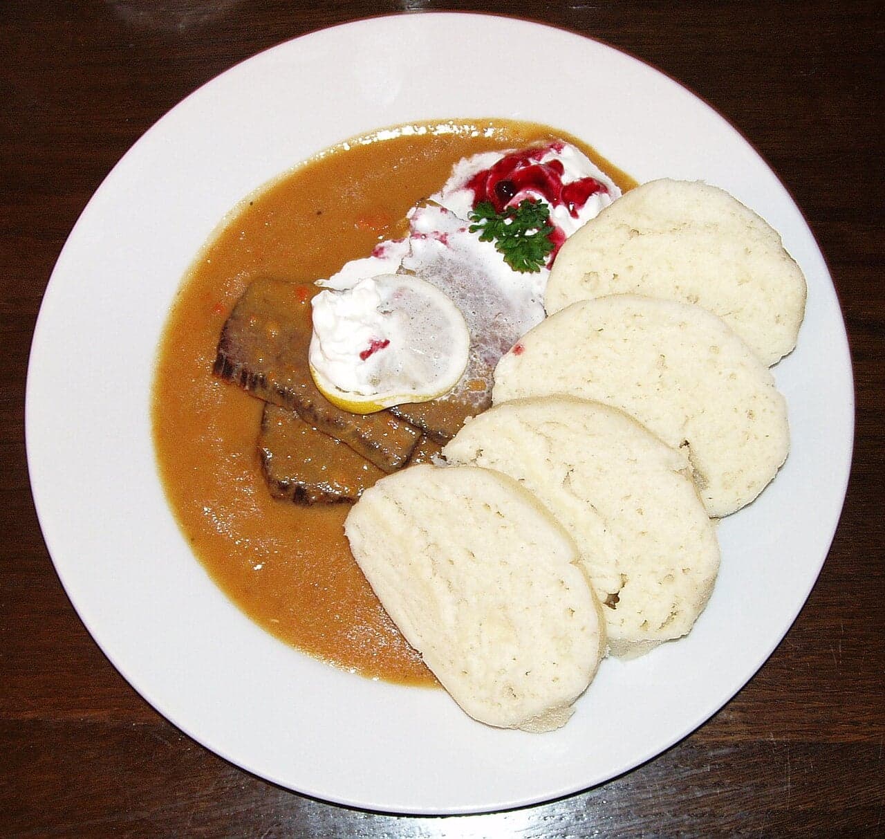 A plate of svíčková - sliced beef in cream sauce with bread dumplings, cranberries and whipped cream