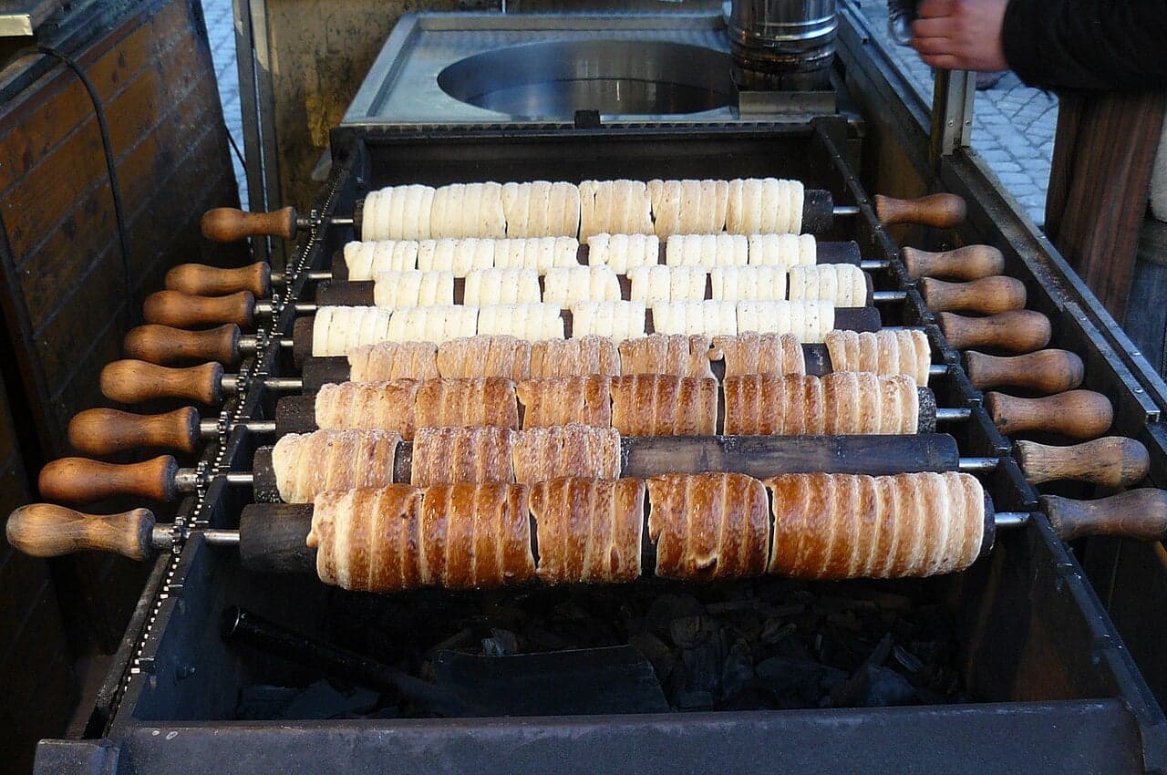 Trdelník pastry rolled in cinnamon sugar being cooked on a wooden spit over flames