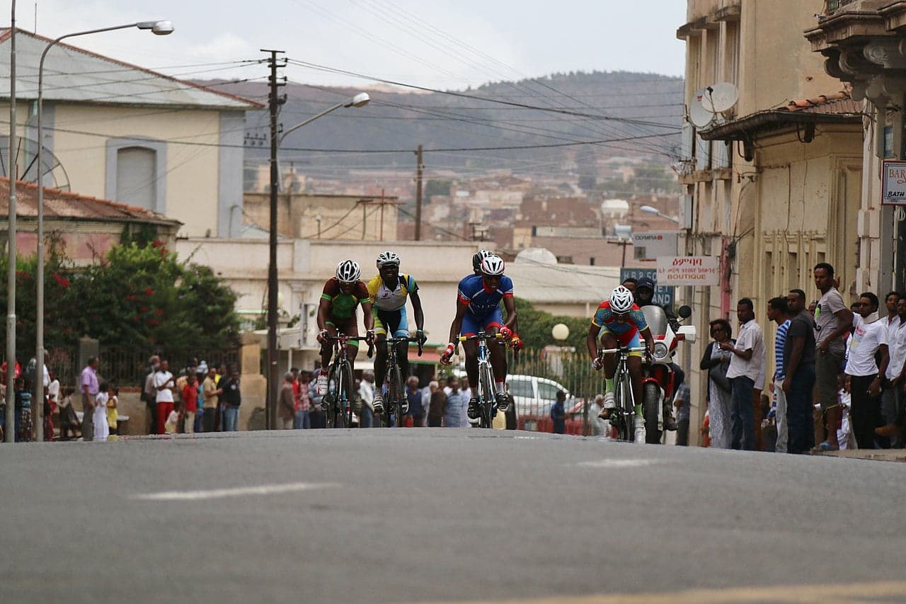 A peloton of cyclists racing up a steep mountain road in the Eritrean highlands with crowds cheering
