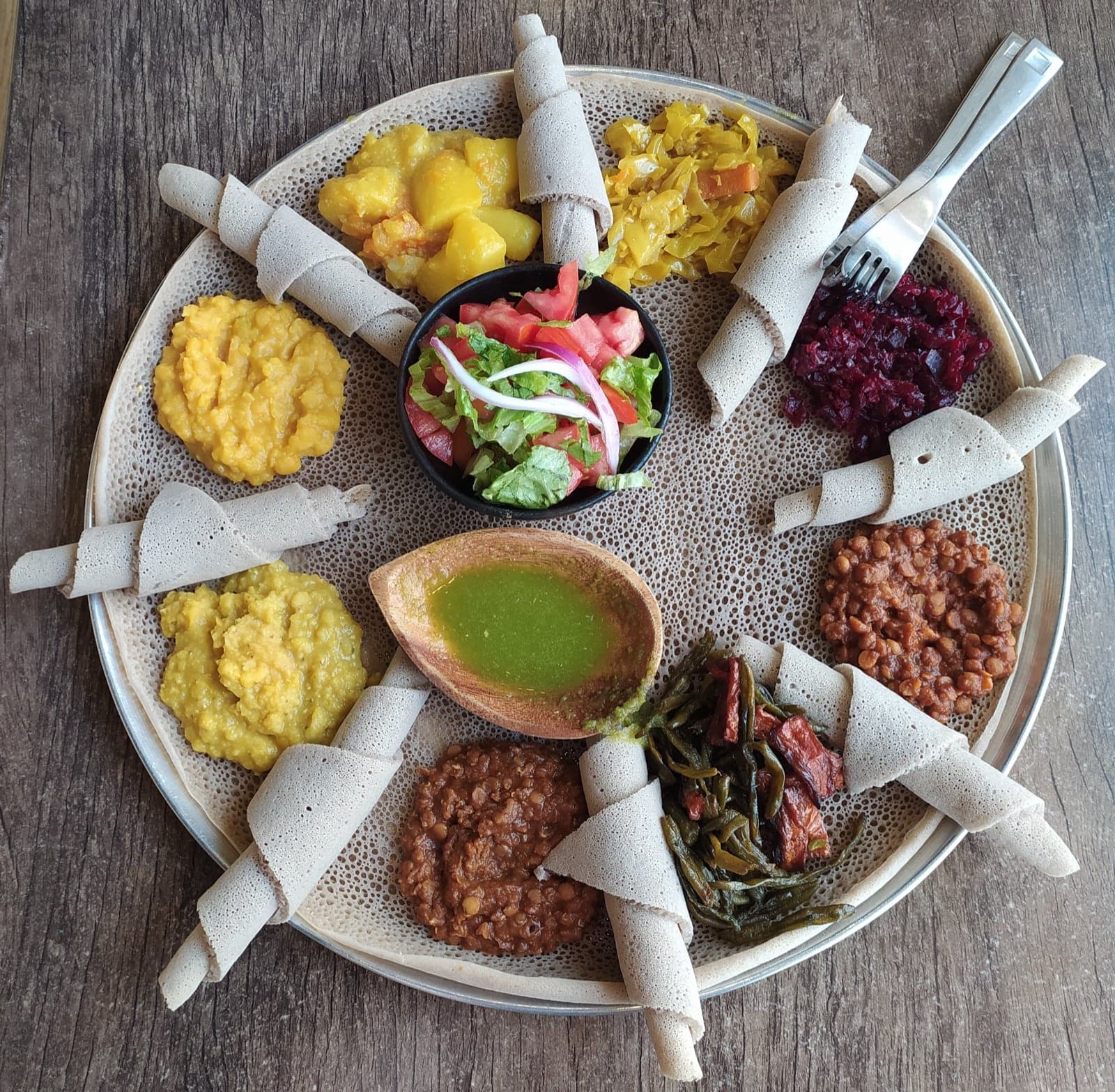 A round injera with several colourful Ethiopian stews placed on top