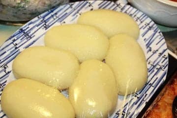 A smooth white ball of fufu on a plate next to a bowl of stew