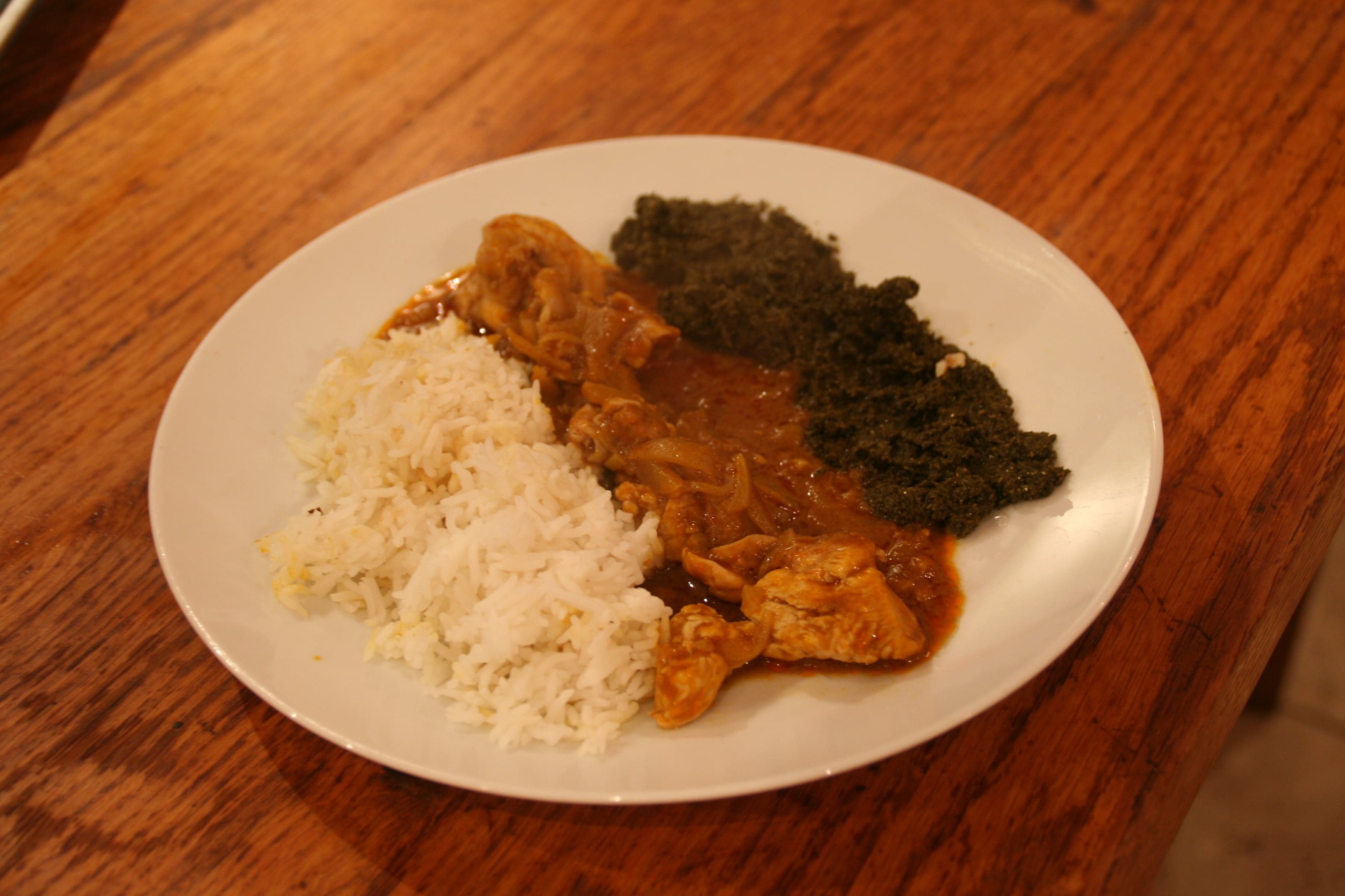A bowl of poulet nyembwe, chicken in a deep orange palm-nut sauce, served with plantain