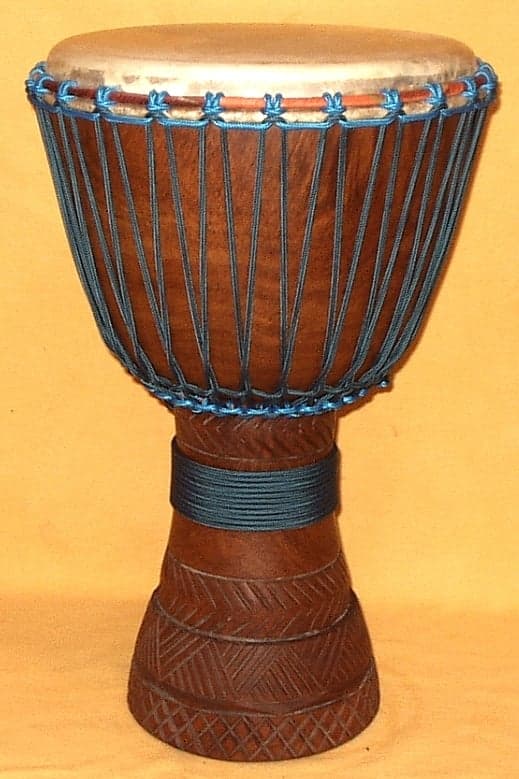 A djembe drum player performing with hands raised above a large goblet-shaped drum