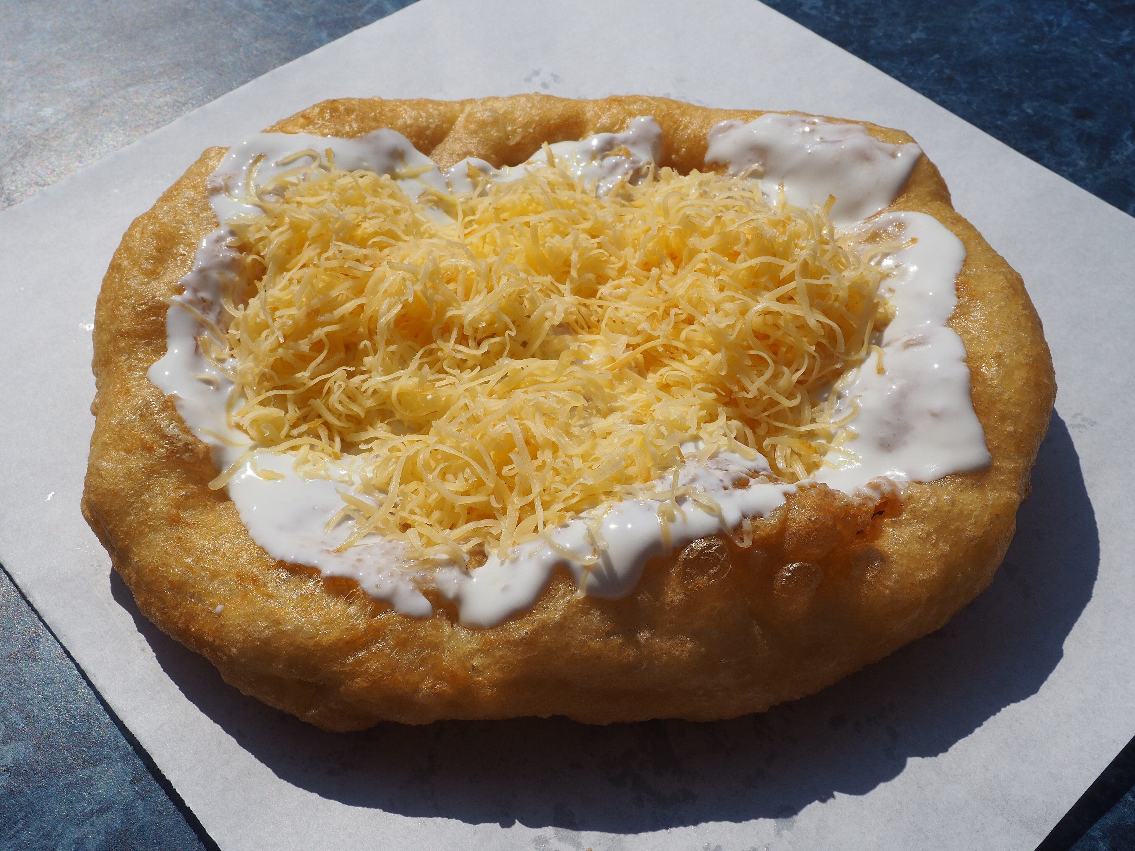 A golden lángos topped with sour cream and grated cheese