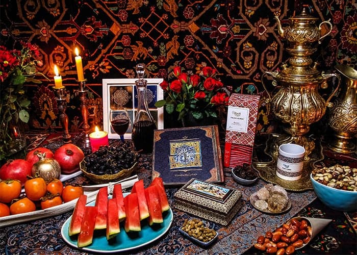 A family gathered around a table spread with pomegranates, watermelon, nuts and candles on a winter evening