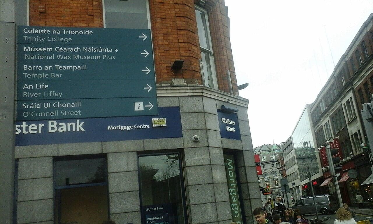 A green road sign in Ireland showing place names in Irish and English