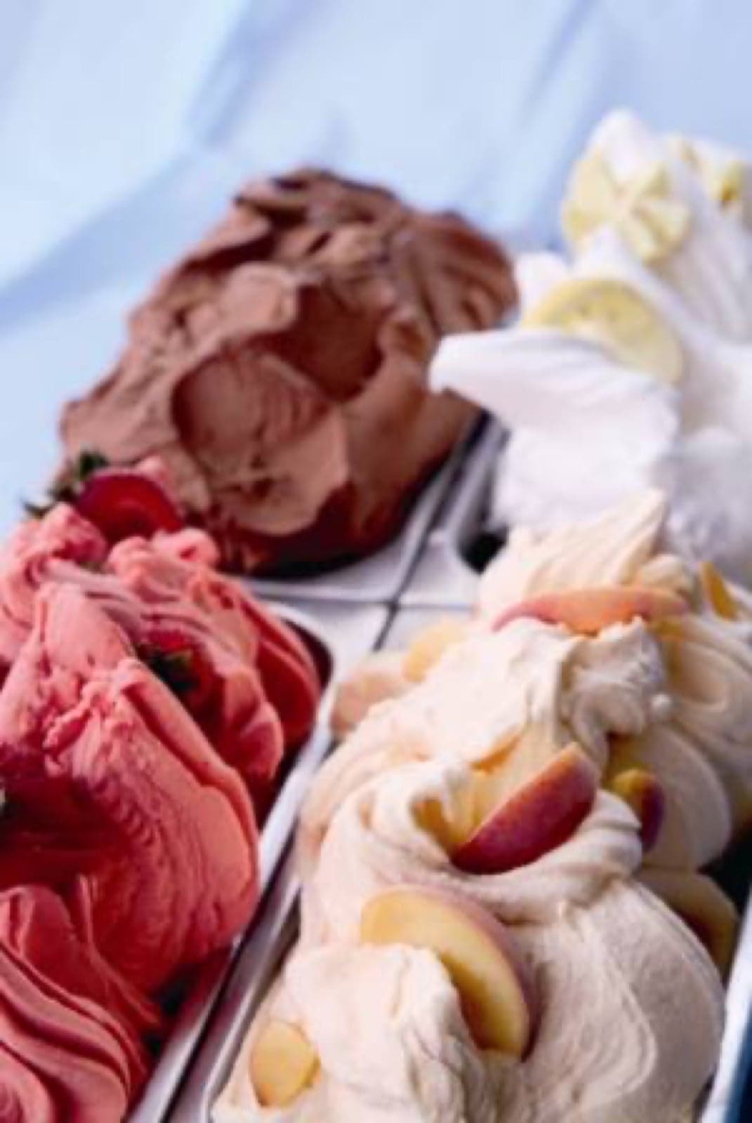 Tubs of pink strawberry, brown chocolate, white vanilla and peach gelato